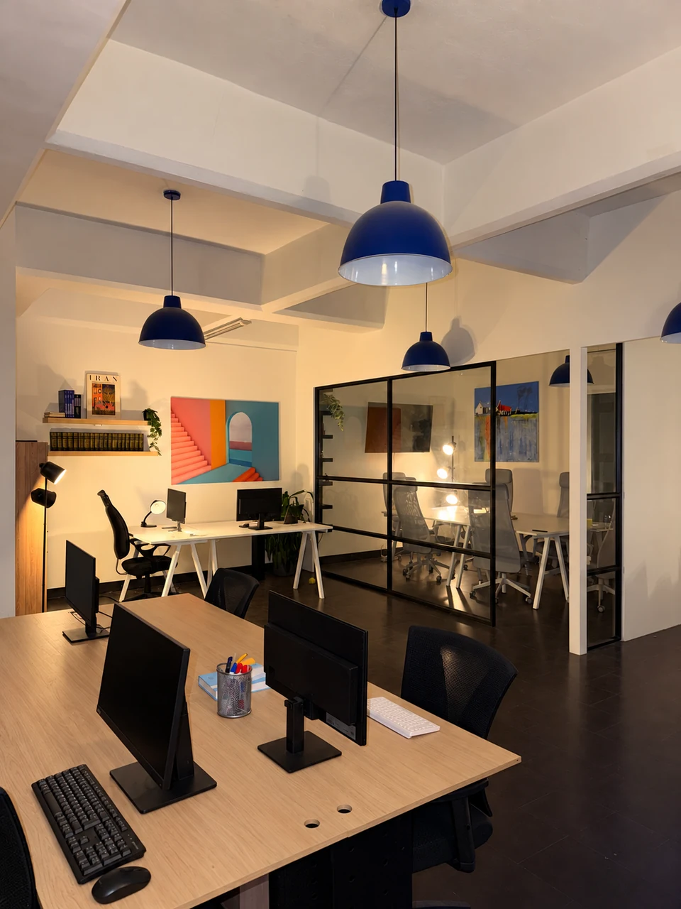 Office interior with workstations, glass partitions and blue pendant lamps